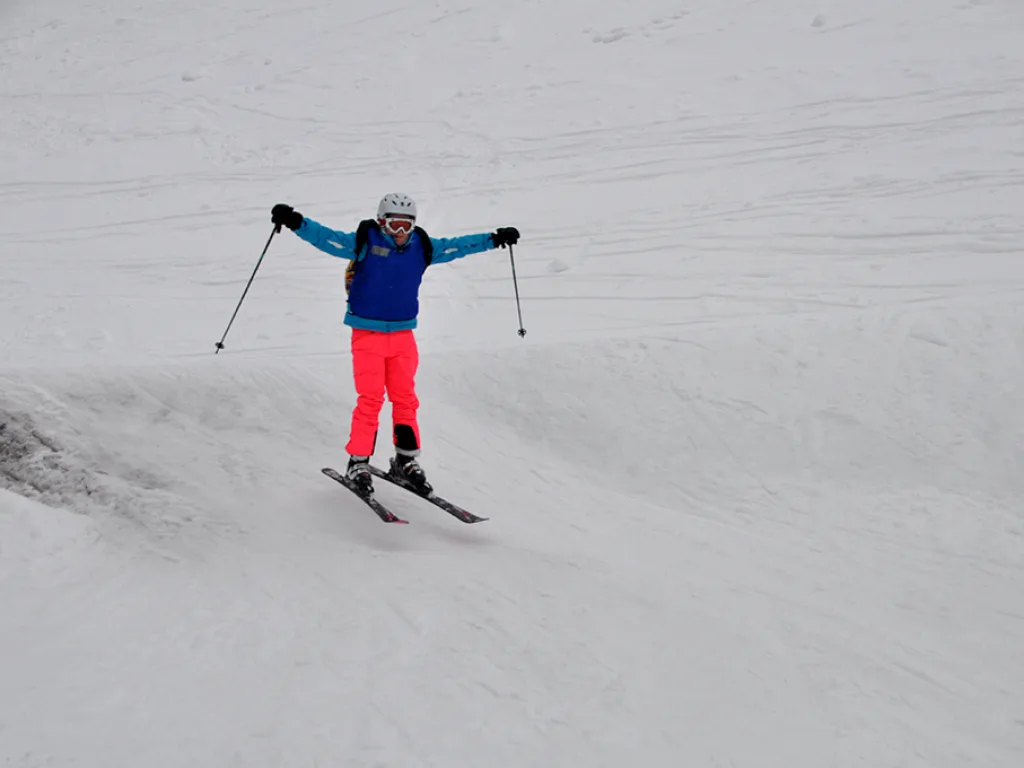 Skifahrerin in pinker Hose springt über eine Kuppe.